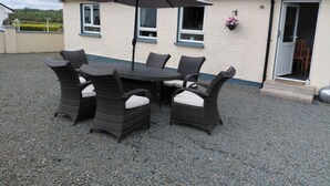 A patio with a table and chairs, a large umbrella, and a house with a grey roof and white walls. - Cottage - Sleeps 6 - Parking (Rathmullan)