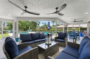 An outdoor patio with wicker furniture, ceiling fans, and a view of a pool and greenery. - Luxurious home wirh private pool in beautiful Delray Beach upscale neighborhood (Delray Beach)