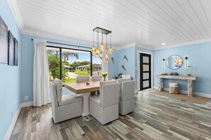 A dining area with a table and chairs, a large window with curtains, and a ceiling with hanging lights. - Luxurious home wirh private pool in beautiful Delray Beach upscale neighborhood (Delray Beach)