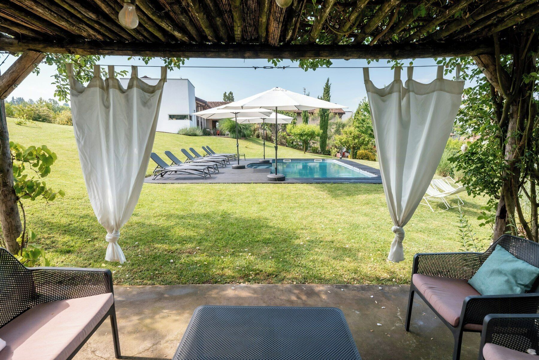 A covered outdoor area with a pool, lounge chairs, and a pergola.