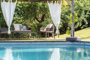 A poolside area with two chairs, a table, and a pergola with white curtains. - Double-house with pool among Barolo vineyards (Novello)