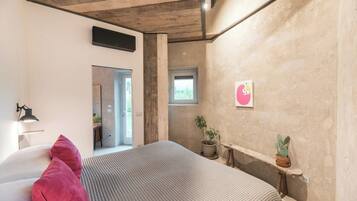 A bedroom with a bed, a potted plant, a small window, and a wall-mounted air conditioner.