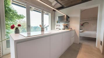 Una cocina moderna con una isla grande, un microondas y un lavamanos. Hay una ventana con vistas a árboles y una cama en la habitación contigua.