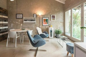 A modern interior with a dining area, two blue chairs, a white table, and a large window. - Design home in the Langhe with pool (Novello)