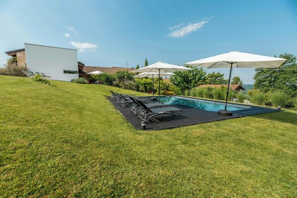 A modern house with a swimming pool, outdoor seating, and a view of the landscape. - Design home in the Langhe with pool (Novello)