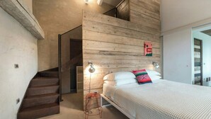 Ein Schlafzimmer mit hölzernem Kopfteil, einem Bett mit weißer Bettwäsche, einem kleinen Hocker und einer Treppe.