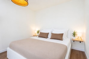 Ein ordentlich bezogenes Bett mit einer beige farbenen Decke, zwei Nachttische mit Lampen und einer Pendelleuchte.