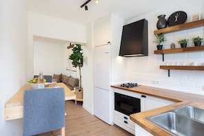 Moderni keittiö, jossa on valkoiset kaapit, puutasot, sisäänrakennettu uuni ja seinälle asennettu musta televisio.