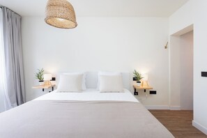 Ein modernes Schlafzimmer mit einem großen Bett, zwei Nachttischen inklusive Lampen, einer gewobenen Deckenleuchte und einem Holzboden.