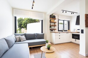 Ein modernes Wohnzimmer mit grauem Sofa, einem runden Couchtisch und einer Küchenzeile mit weißen Schränken und einem schwarzen Backofen.