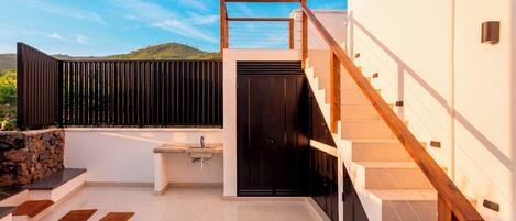 A modern outdoor kitchen area with a sink, a black door, and a staircase leading to an upper level.