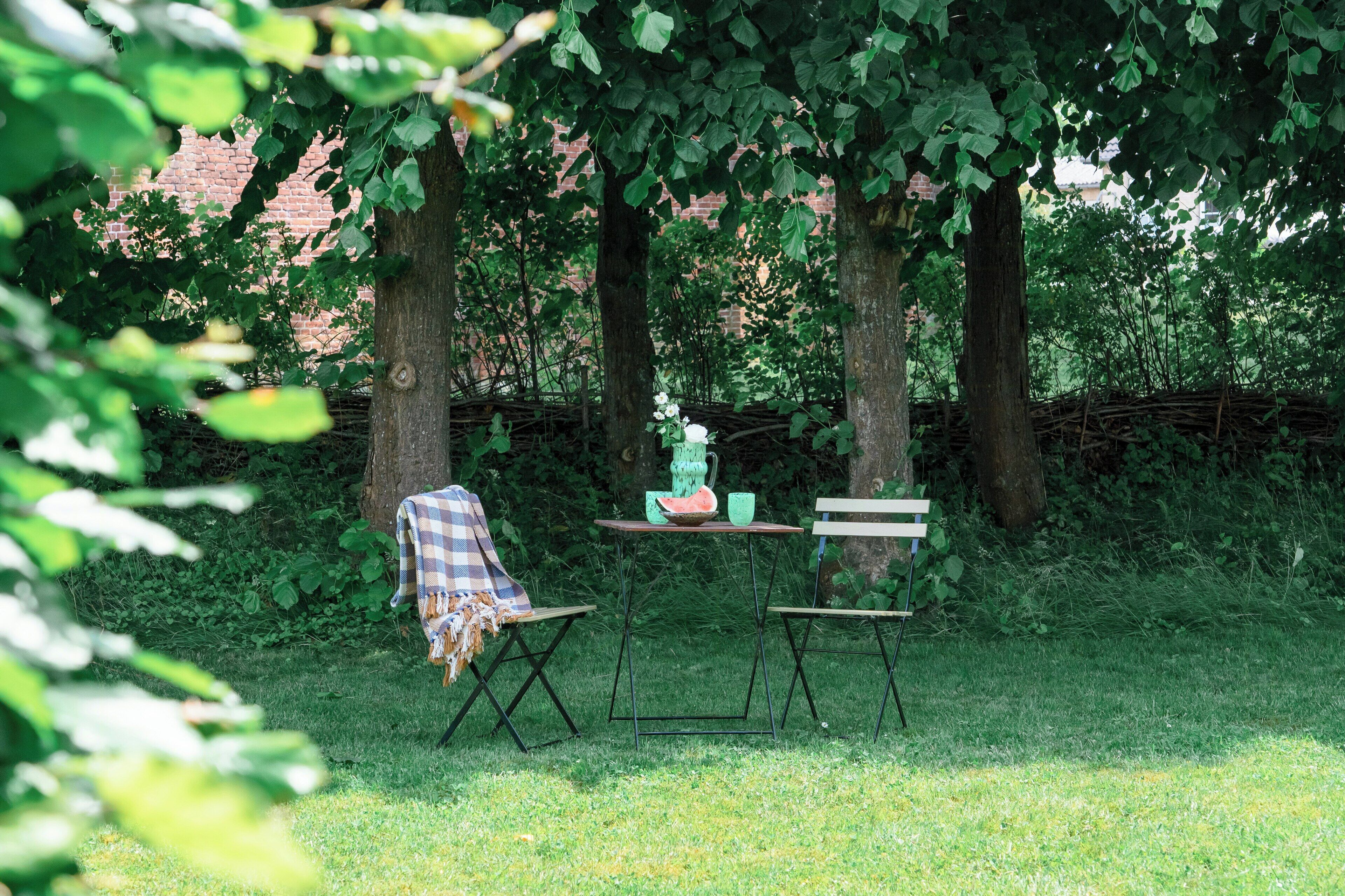 Un espace extérieur aménagé avec une table et des chaises, entouré d’arbres et d’un mur de briques.