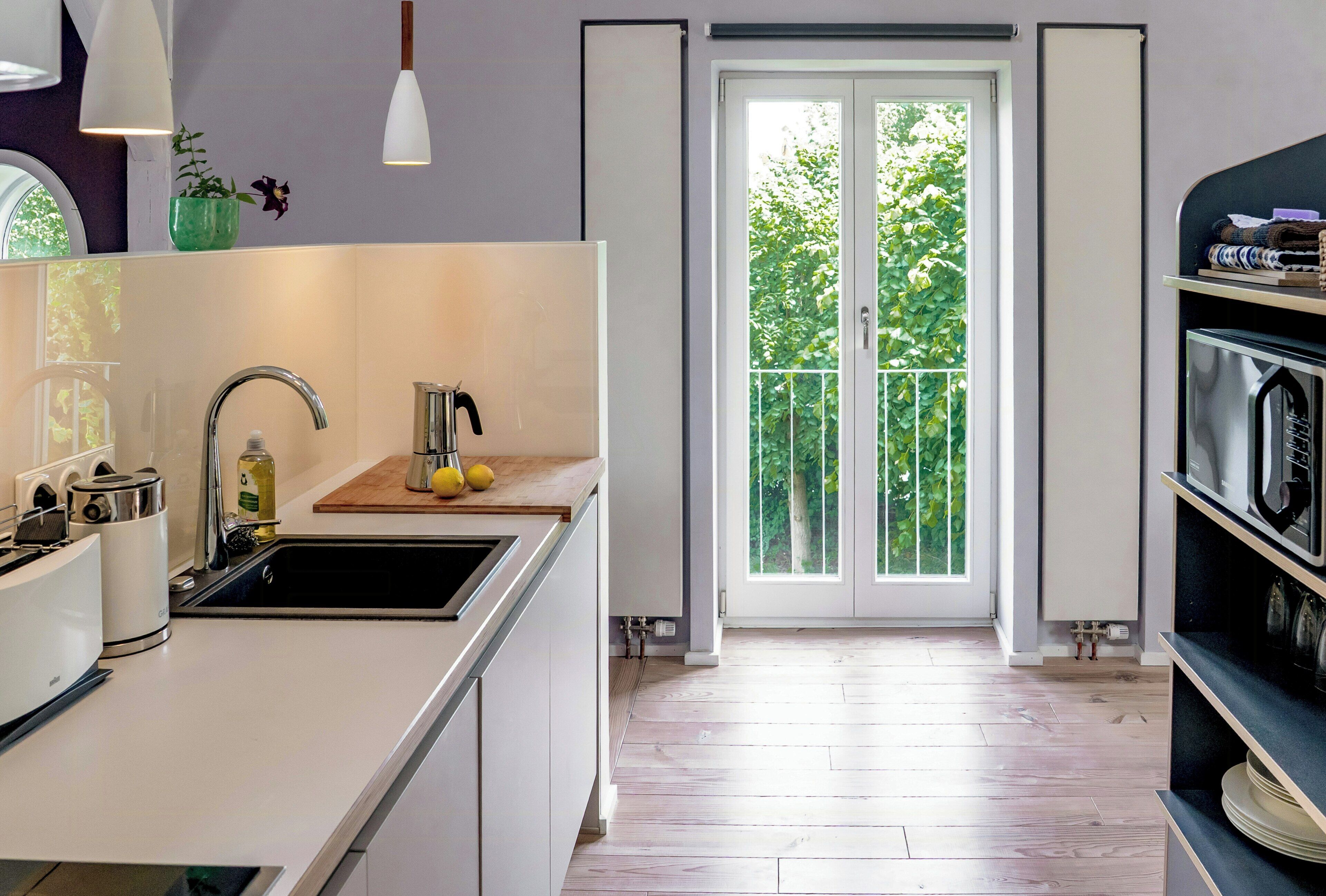 A modern kitchen with a sink, a wooden countertop, and a view of a balcony with greenery.