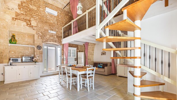 Un'ampia cucina con zona pranzo, una scala e una parete in pietra.