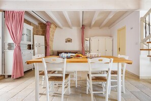 Ein Essbereich mit Holztisch und weißen Stühlen, eine Küche mit Steinwand und eine Treppe.