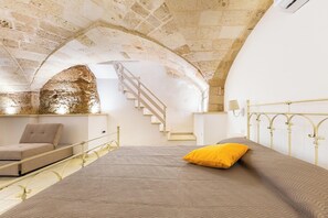 Ein Schlafzimmer mit Bett, Stuhl, Treppe und Steinwand.