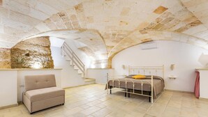 Una camera da letto con soffitto in pietra, un letto con struttura in metallo, un divano e una scala.