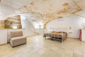 Ein Schlafzimmer mit Steindecke, einem Bett mit Metallgestell, einer Couch und einer Treppe.
