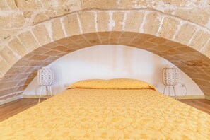 Ein Zimmer mit einer Decke aus Ziegelgewölbe, einem Bett mit gelbem, gemusterten Bettbezug und je einer weißen Lampe auf beiden Seiten des Bettes.