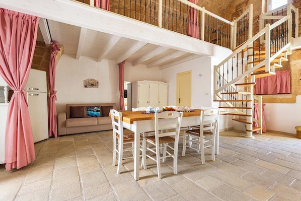 Ein Essbereich mit einem Holztisch und weißen Stühlen, eine Treppe mit Geländer aus Holz und ein beiges Sofa im Hintergrund.