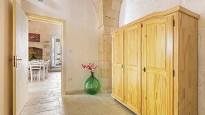 A hallway with a stone wall, a wooden cabinet, and a green vase with flowers. - La Vecchia Grotta - Trilo Comfort by BarbarHouse (Maruggio)