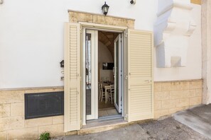 Entrada de un edificio con una puerta abierta que muestra un área de comedor con sillas y una mesa.