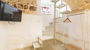 A room with a TV mounted on the wall, a staircase, and a wooden bench. - La Vecchia Grotta - Trilo Comfort by BarbarHouse (Maruggio)