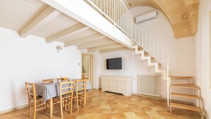 A dining area with a table and chairs, a staircase, a television, and a radiator. - La Vecchia Grotta - Appartamento by BarbarHouse (Maruggio)