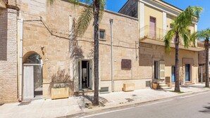 A stone building with balconies, a paved sidewalk, and palm trees. - La Vecchia Grotta - Appartamento by BarbarHouse (Maruggio)