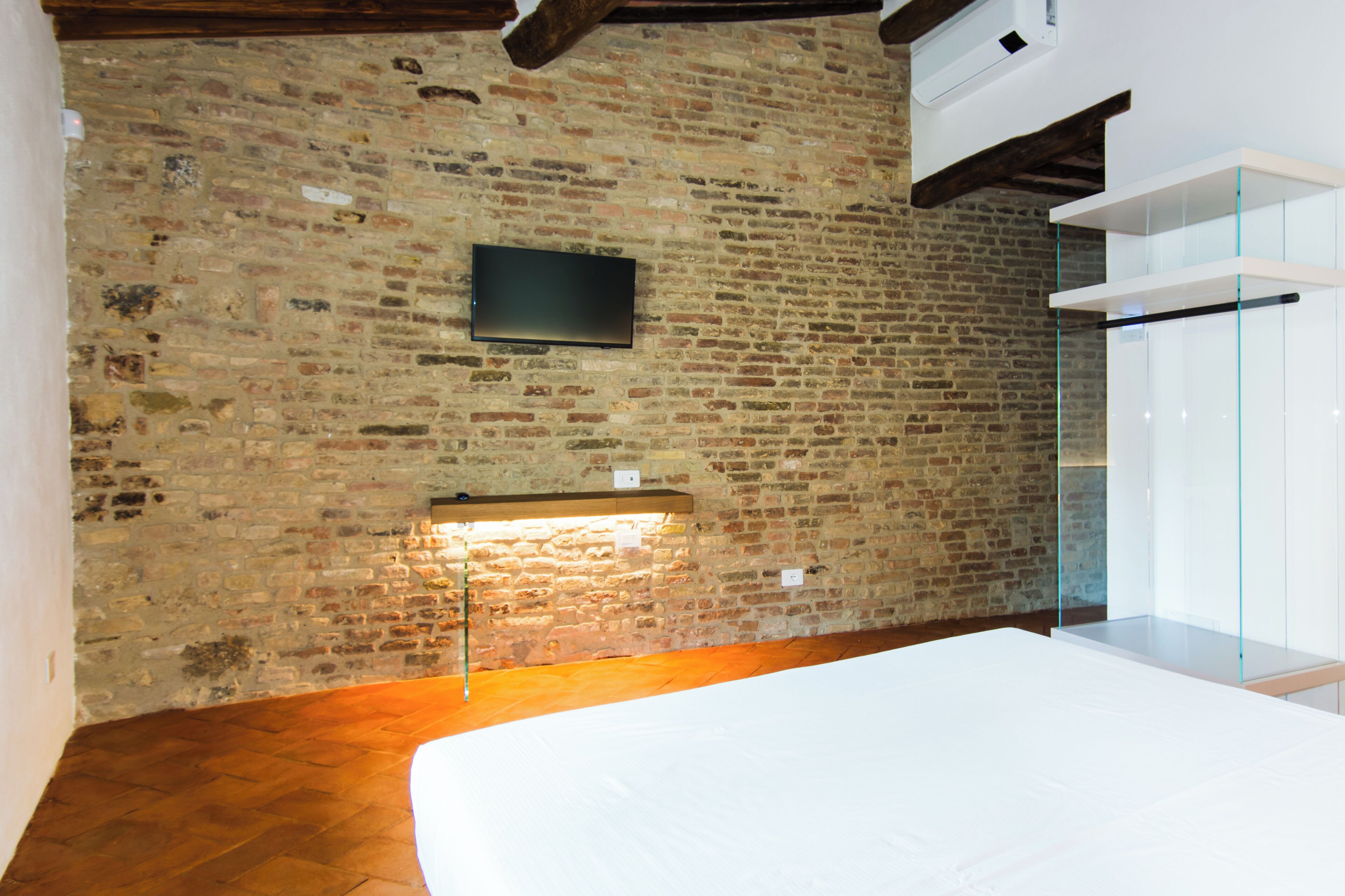 A room with exposed brick walls, a flat-screen TV mounted on the wall, a wooden floor, and a glass partition.