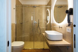 Un baño moderno con ducha de vidrio, lavamanos blanco y un secador de pelo portátil fijado en la pared.