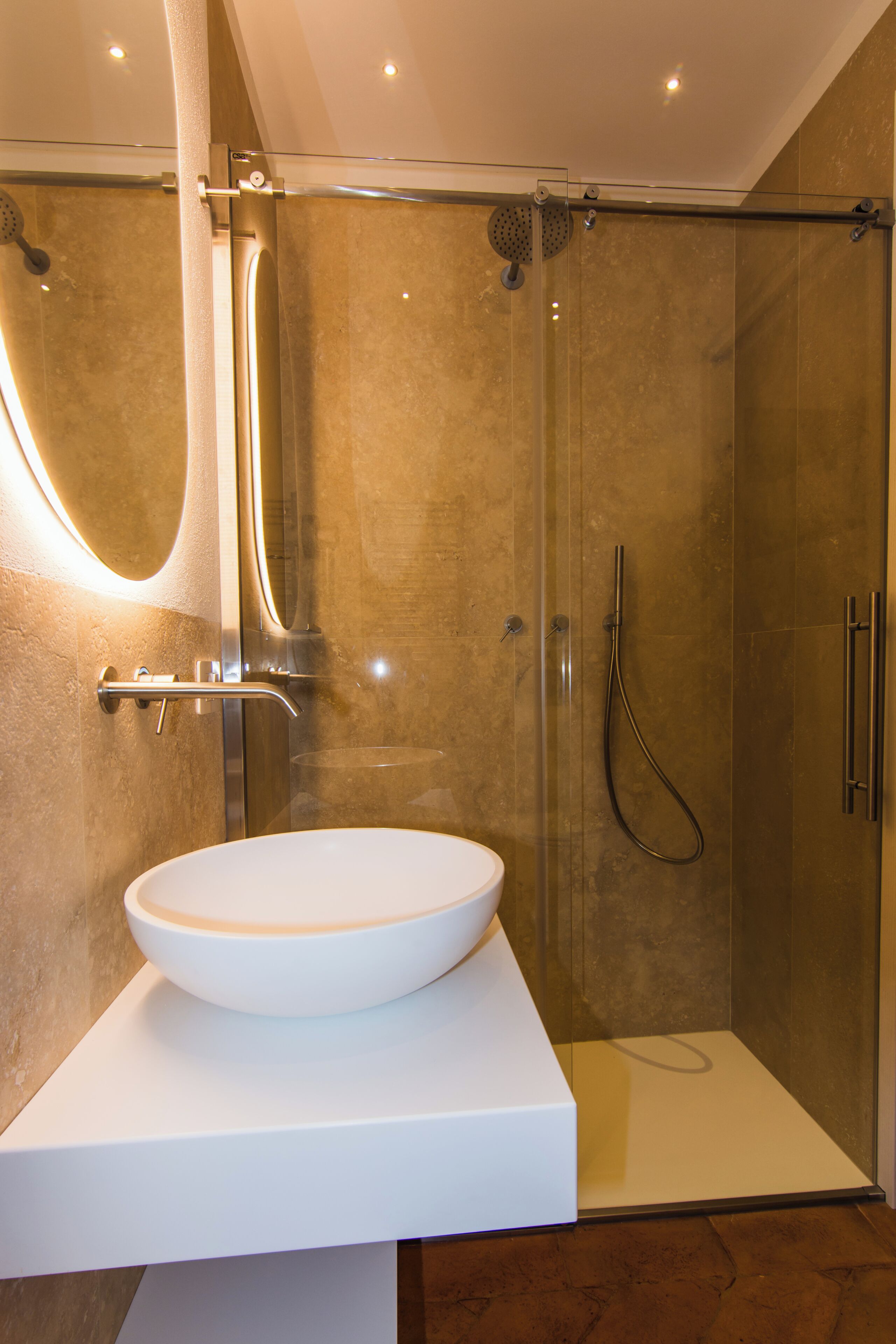 Ein modernes Badezimmer mit einer einteiligen Glasdusche, einem weißen Waschbecken und einer marmorierten Wand.
