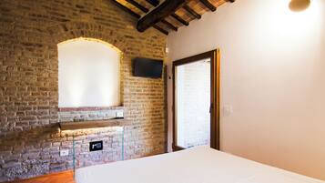 A room with a brick wall, a flat-screen TV mounted above a fireplace, a bed, and a door.