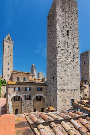 A historic stone building with a prominent tower, arched windows, and a tiled roof. - Materia Rooms San Gimignano (San Gimignano)