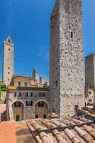 Un edificio histórico de piedra con una torre destacada, ventanas arqueadas y techo de tejas.