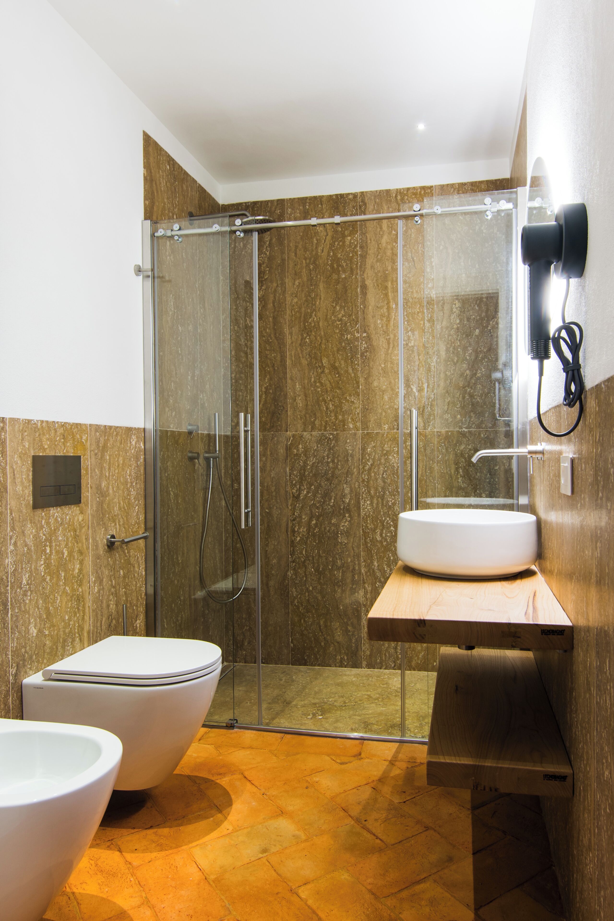 Ein modernes Badezimmer mit einer gläsernen Duschkabine, einem weißen Waschbecken und zwei Toiletten.