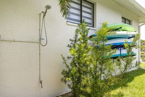 Ein weißes Gebäude mit Dusche, einem Fenster mit Jalousien und einem grünen Kajak auf einem Ständer.