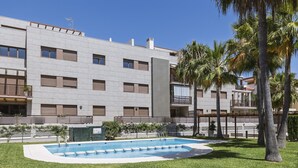 A modern building with a swimming pool, surrounded by well-maintained grass and palm trees. - Piso de dos dormitorios en planta baja con acceso directo al jardín y piscina (Javea)