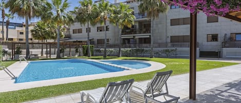 A swimming pool with lounge chairs, palm trees, and a building with balconies.