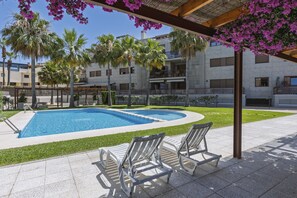 Una piscina con sillas de descanso, palmeras y un edificio con balcones.