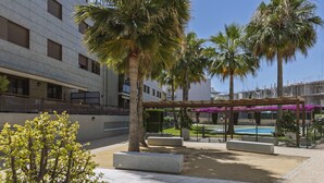 A courtyard with palm trees, a pool, and a covered seating area. - Piso de dos dormitorios en planta baja con acceso directo al jardín y piscina (Javea)