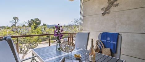 A balcony with a table set for two, a bottle of champagne, a bowl of snacks, and a decorative wall piece.
