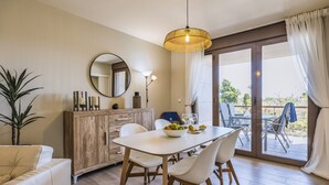 A dining area with a white table, chairs, a wooden cabinet, a mirror, and a hanging light fixture. - Piso de dos dormitorios en planta baja con acceso directo al jardín y piscina (Javea)