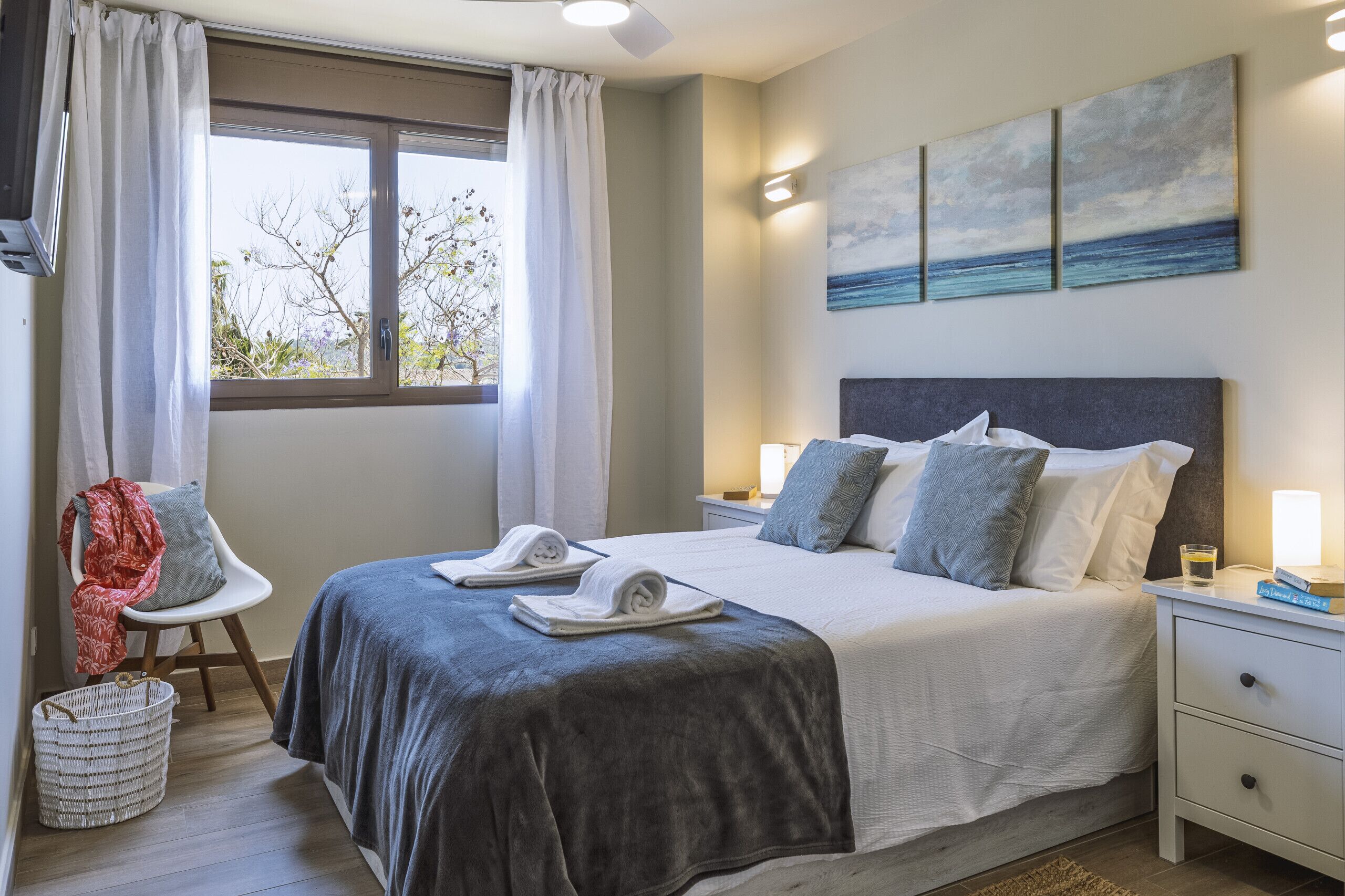 Quarto bem organizado com cama, mesas de cabeceira, uma cadeira e janela com cortinas.