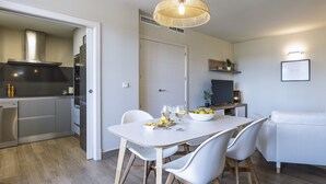 A modern kitchen with white cabinets, a dining table with white chairs, and a white sofa in the living area. - Piso de dos dormitorios en planta baja con acceso directo al jardín y piscina (Javea)