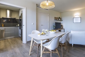Eine moderne Küche mit weißen Schränken, ein Esstisch mit weißen Stühlen und ein weißes Sofa im Wohnbereich.