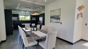 Un espace repas moderne avec une longue table, des chaises blanches et une cuisine en arrière-plan.