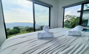 Habitación de hotel con una cama grande, dos toallas enrolladas y vistas a montañas y vegetación.
