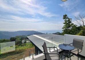 Un balcón con mesa y sillas, barandilla de vidrio y vistas al paisaje.