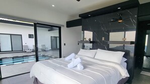 Une chambre moderne avec un grand lit, une porte vitrée donnant sur un balcon et un grand miroir au mur.